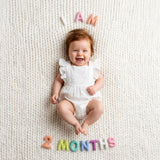 Pastel Felt Milestone Numbers spelling "I AM 2 MONTHS" arranged around a laughing baby on a cream knit blanket.