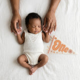 1-month milestone photo with mom's hands and Flower Child pennant