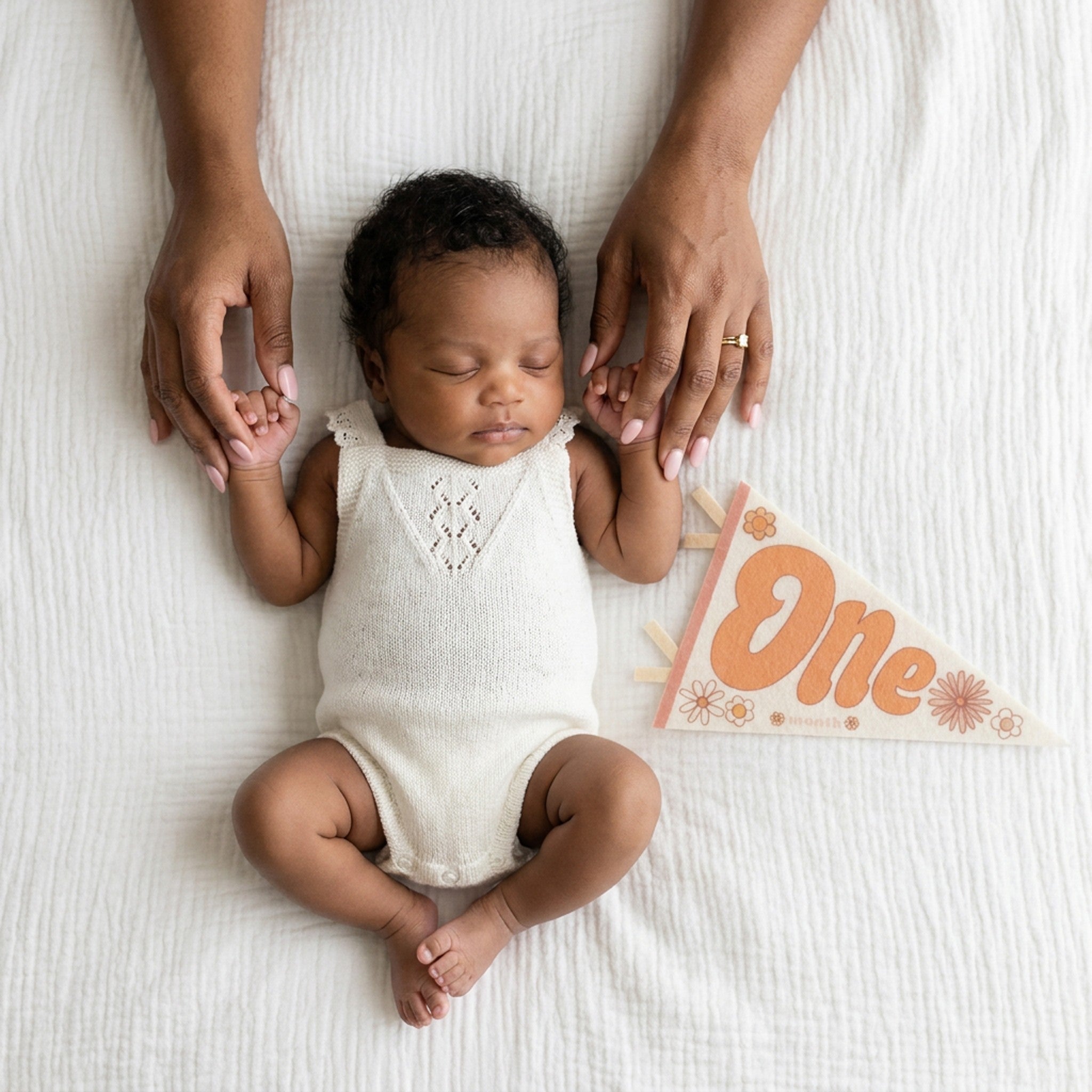 1-month milestone photo with mom's hands and Flower Child pennant