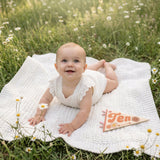 10-month milestone photo in a daisy meadow with Flower Child pennant