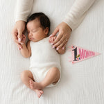 1-month milestone photo with mom's hands and Little Artist pennant