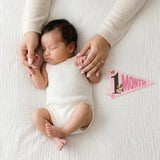 1-month milestone photo with mom's hands and Little Artist pennant