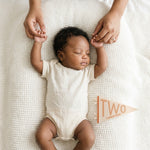 2-month milestone photo with mom's hands and Mountain Fields pennant