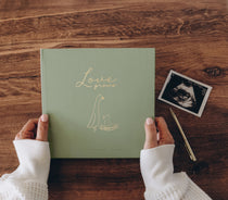 Hands holding the Lucy Darling Pregnancy Journal in Moss Green with a gold-foil Love Grows cover